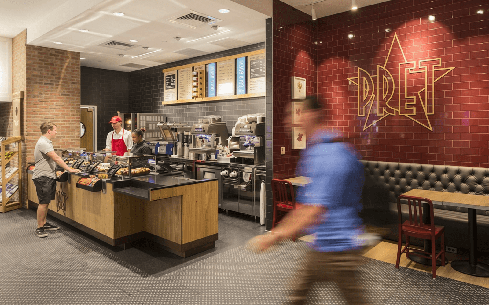 A Pret A Manger store at service — the counter, the kitchen behind it, and the brand mark on the back wall